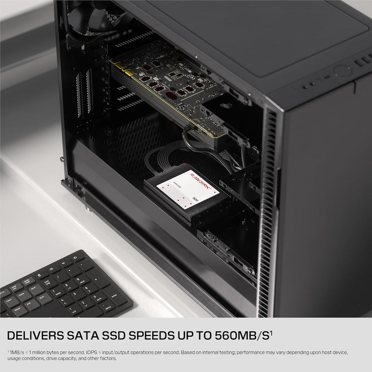 A black computer case shown open, revealing internal components including a graphics card and a hard drive, on a light gray surface with a keyboard partially visible. Text at the bottom states it delivers SATA SSD speeds up to 560MB/s.